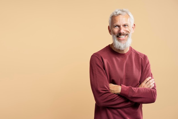 Foto un bel uomo barbuto e sorridente che tiene le braccia incrociate e guarda lontano isolato sullo sfondo.