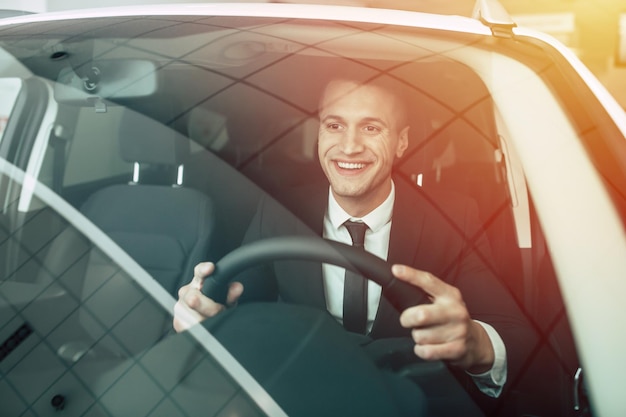 Handsome smiling business man driving a car Man in fullsuit buying car in dealership