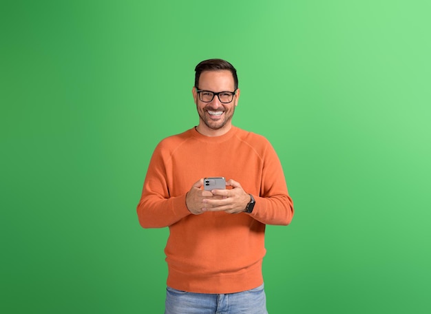 Handsome smiling businessman in eyeglasses messaging over smart phone on isolated green background