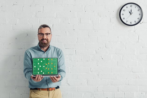 Handsome and smiling businessman holding laptop with football website