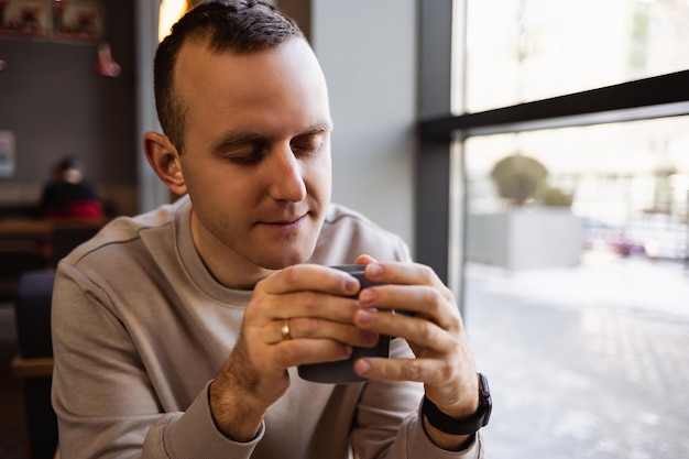 Un bel giovane sorridente e calmo siede in un bar a un tavolo bevendo caffè mentre è seduto a un tavolo in un ristorante caffè mattutino