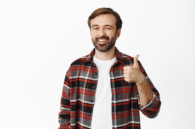 Handsome smiling family man winking and showing thumbs up recommending product praise and like promo offer standing over white background