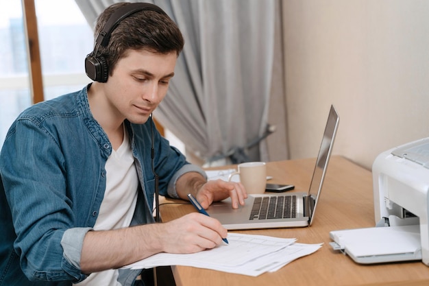 Photo handsome smiling guy doing homework and enjoying studying online