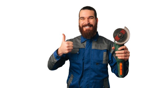 Foto l'uomo pratico sorridente bello sta tenendo una smerigliatrice angolare e un pollice in su