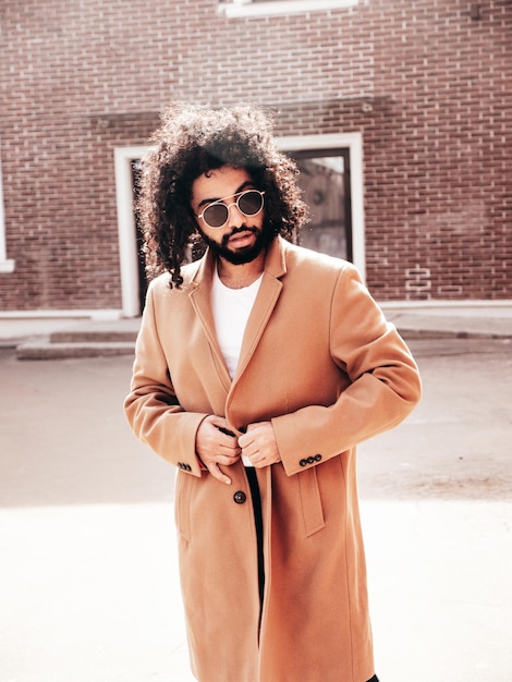 Handsome smiling hipster model Arabian man dressed in brown coat outdoors in street