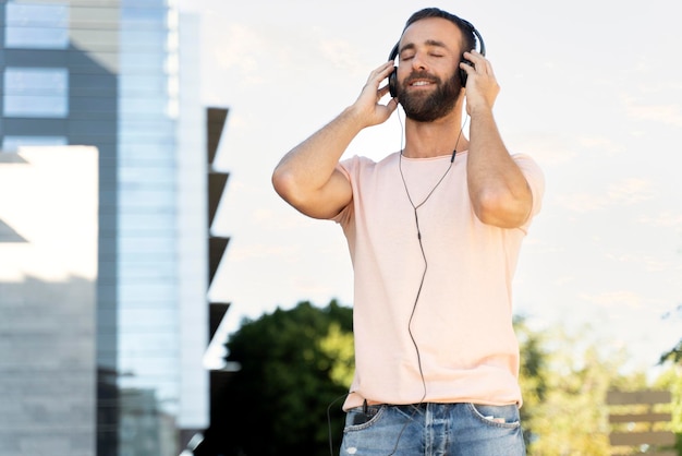 ハンサムな笑顔のラテン男が目を閉じて通りに立ち、コピースペースで音楽を聴く