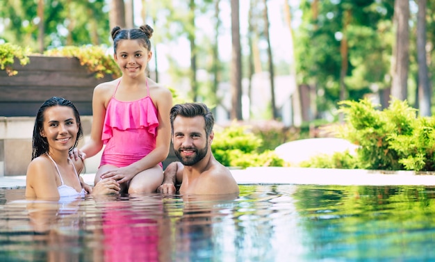 Foto bell'uomo sorridente e carina donna eccitata con loro piccola adorabile figlia si divertono nella piscina estiva mentre riposa in hotel.