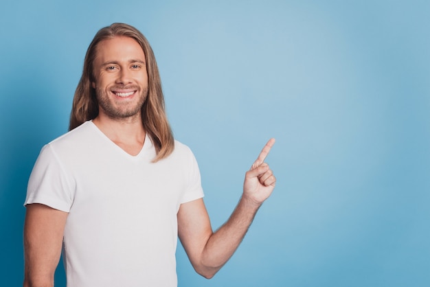 Handsome smiling man pointing finger emptyspace on blue background.