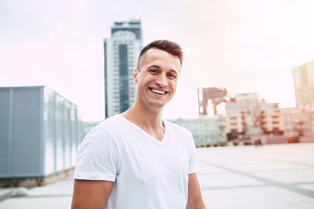 Bell'uomo sorridente in abbigliamento sportivo in piedi su uno sfondo di paesaggio urbano dopo aver fatto jogging