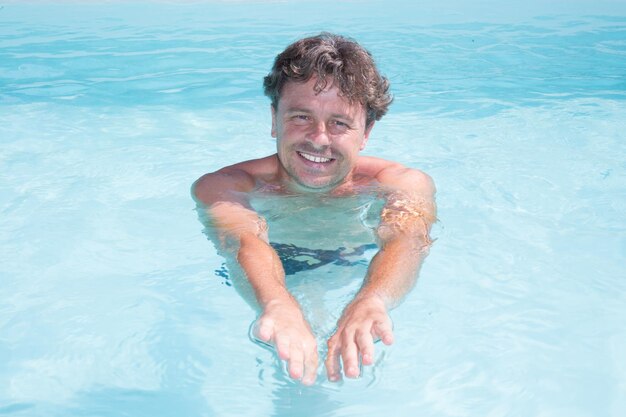 Handsome smiling man in swimming pool in summer scenery