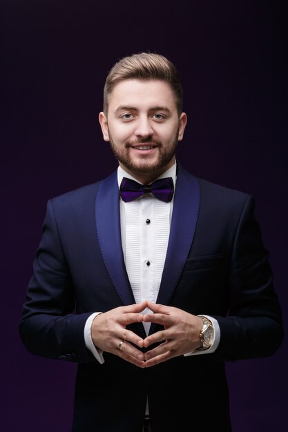 Handsome smiling man in tuxedo and bow tie looking at camera fashionable festive clothing emcee on dark