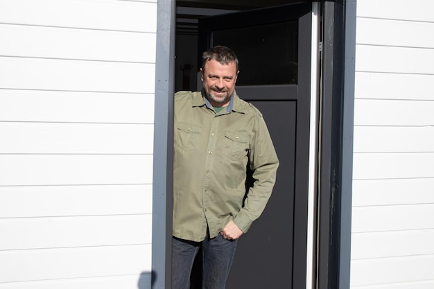 Handsome smiling middle aged man posing on open home door