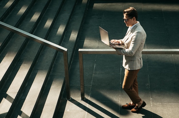 Handsome smiling young business man spending time outdoors at the city using laptop computer on stairs