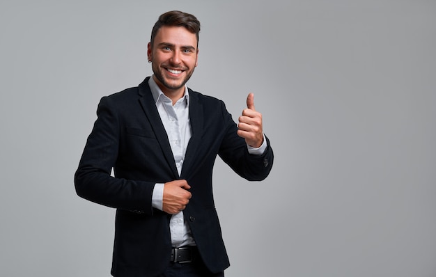 Handsome smiling young businessman showing thumbs up