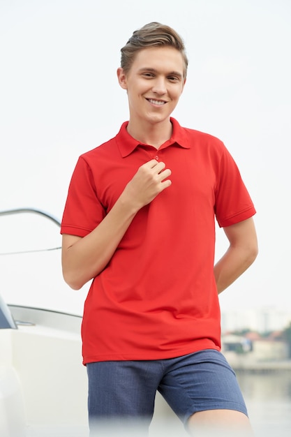 Handsome smiling young man standing on luxurious yacht he\
rented for summer vacation