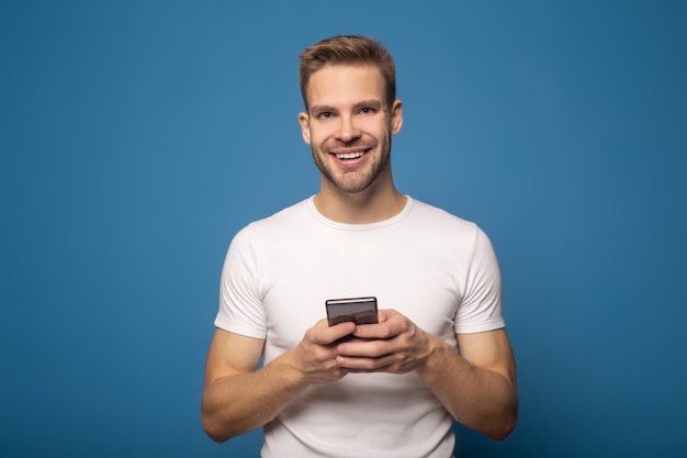 Handsome smiling young man using smartphone isolated on blue