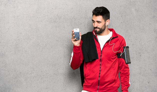 Handsome sportman with troubled holding broken smartphone over textured wall