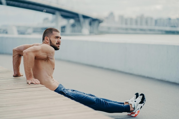 ハンサムなスポーツマンは、筋肉を鍛え、背中の腕立て伏せの練習を行い、屋外でウォーミングアップしてから、集中して走る前に、筋肉質の体がアクティブな健康的なライフスタイルをリードし、筋肉質の胴体がむき出しになっています