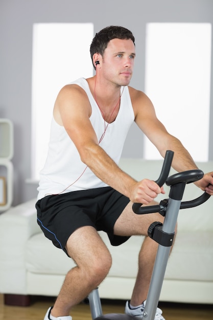 Handsome sporty man exercising on bike and listening to music