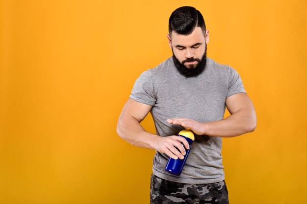 Handsome strong man drinks water on yellow background