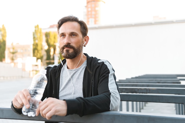 Handsome strong mature sportsman holding bottle with water.