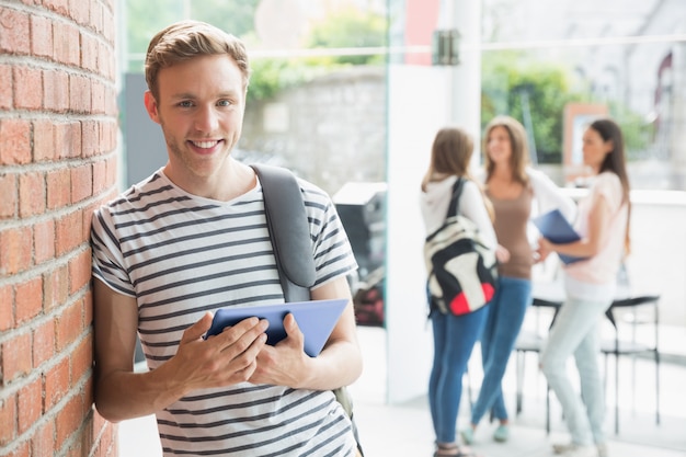 Handsome student smiling and holding tablet