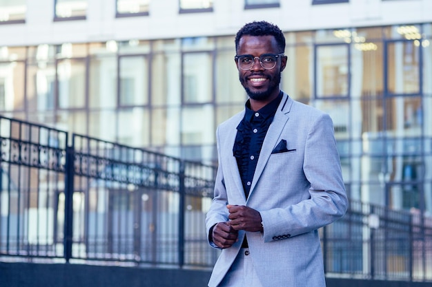 Handsome and stylish afro american businessman in a fashionable jacket and a white shirt with a collar background of Manhattan glass offices cityscape