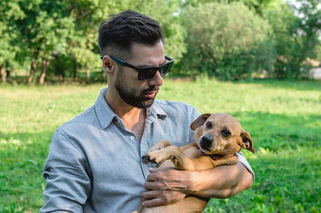 handsome stylish european man is holding his dog in hands in park on a walk