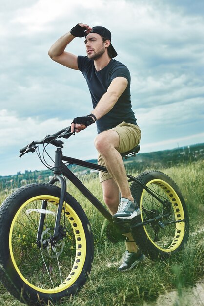 Handsome stylish guy cycling at the mountains and looks far away bottom view