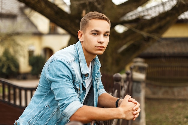 Handsome stylish man in jeans clothes and a white T-shirt near a house in the garden