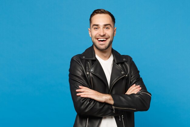 Handsome stylish young bearded man in black leather jacket white t-shirt looking camera isolated on blue wall background studio portrait. People sincere emotions lifestyle concept. Mock up copy space.