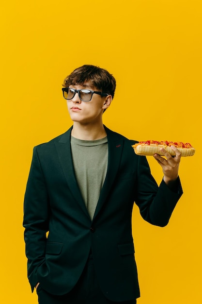 Красивый стильный молодой человек позирует на цветном фоне с хот-догом