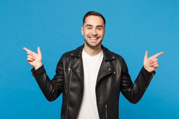 Handsome stylish young unshaven man in black jacket white t-shirt showing on workspace isolated on blue wall background studio portrait. People sincere emotions lifestyle concept. Mock up copy space.