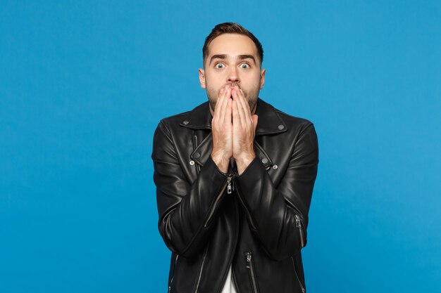 Handsome stylish young unshaven man in black leather jacket white t-shirt looking camera isolated on blue wall background studio portrait. People sincere emotions lifestyle concept. Mock up copy space