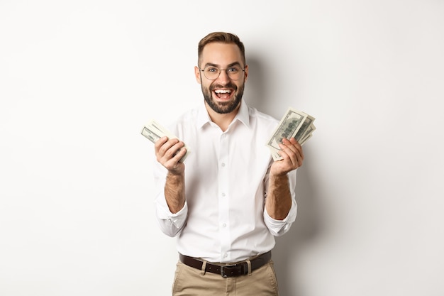 Photo handsome successful business man counting money, rejoicing and smiling, standing over white background.