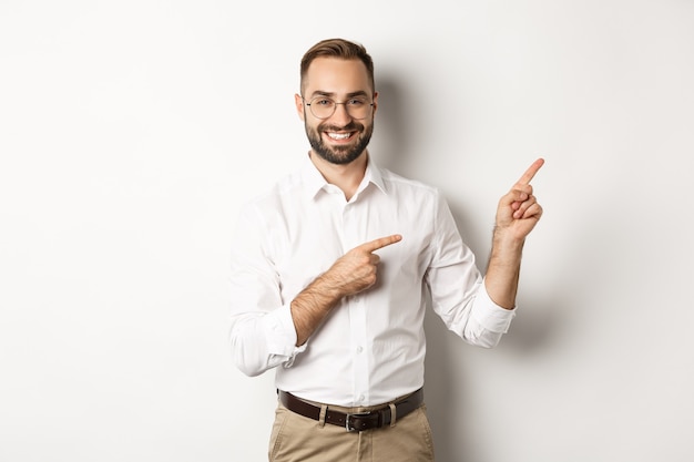 Handsome successful businessman pointing fingers right, showing advertisement with pleased face, white background