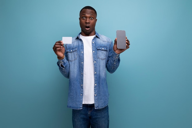 Handsome surprised young attractive african man dressed casually in denim clothes holding credit