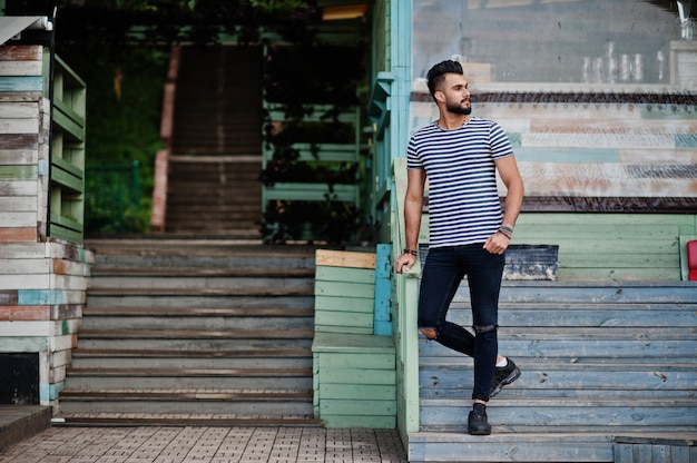 Handsome tall arabian beard man model at stripped shirt posed outdoor. Fashionable arab guy.