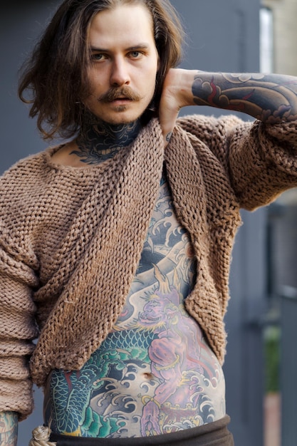 красивый татуированный сексуальный мужчина с длинными волосами и усами в вязаном свитере. Портрет снаружи крупным планом.