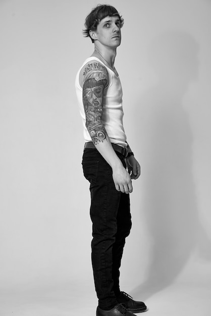 Handsome tattooed young man in white tshirt standing against light background in studio shot