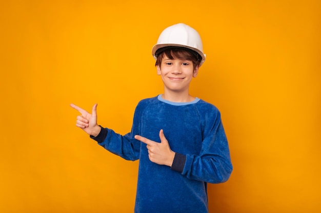 Handsome teen boy wearing white hard protection hat is pointing aside