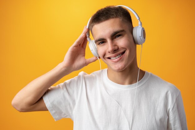 Handsome teenage boy with headphones on head against yellow background