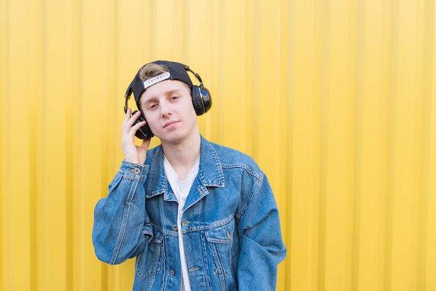 Handsome teenage man stands with headphones on a lively wall