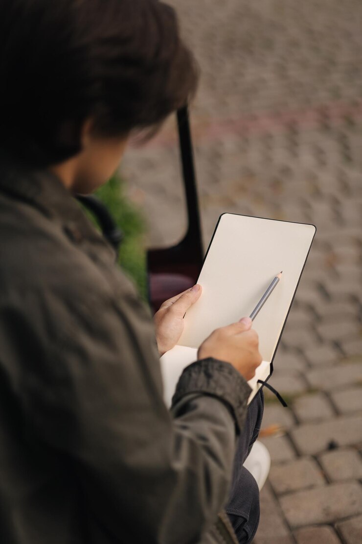 彼のメモ帳に何かを描いているハンサムなティーンエイジャーは、休憩中に才能のある少年を凌駕しました