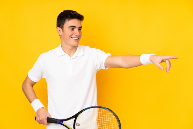 Handsome teenager tennis player man isolated on yellow background playing tennis