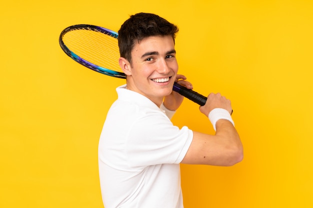 Handsome teenager tennis player man isolated on yellow background playing tennis