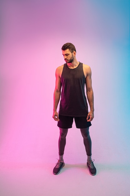 Handsome thoughtful bearded european young man. Front view of guy wear tank top. Isolated on blue and pink background. Studio shoot. Copy space