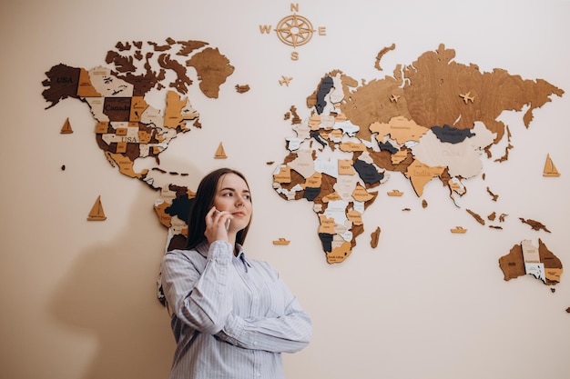 Handsome travel agent standing in the office and talking on the phone on the background of a world map