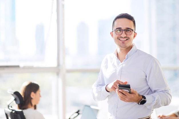Красивый турецкий мужчина улыбается и проверяет свой мобильный телефон в современном офисе