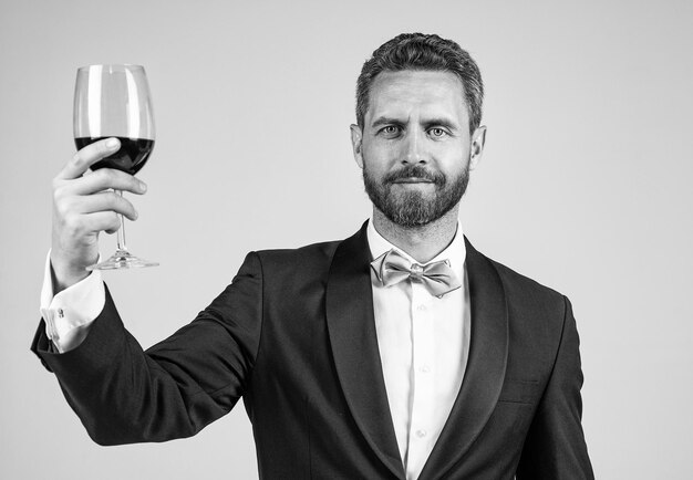 Handsome tuxedo man in bow tie cheers with glass of red wine anniversary